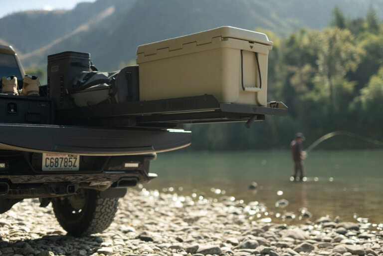 A cooler sits on a an extended TruckGlide Half Width system while a fisherman fishes in the background
