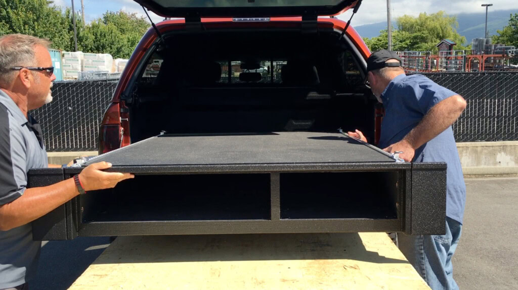 Two men with careers at TruckVault install a drawer system into a vehicle.
