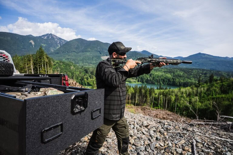 Man shoots rifle next to an open All Weather TruckVault drawer